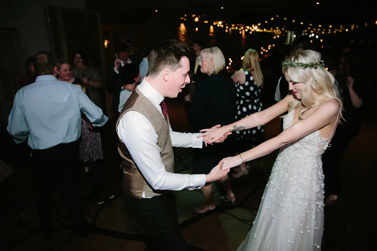 Bride and groom holding hands and dancing among guests under fairy lights
