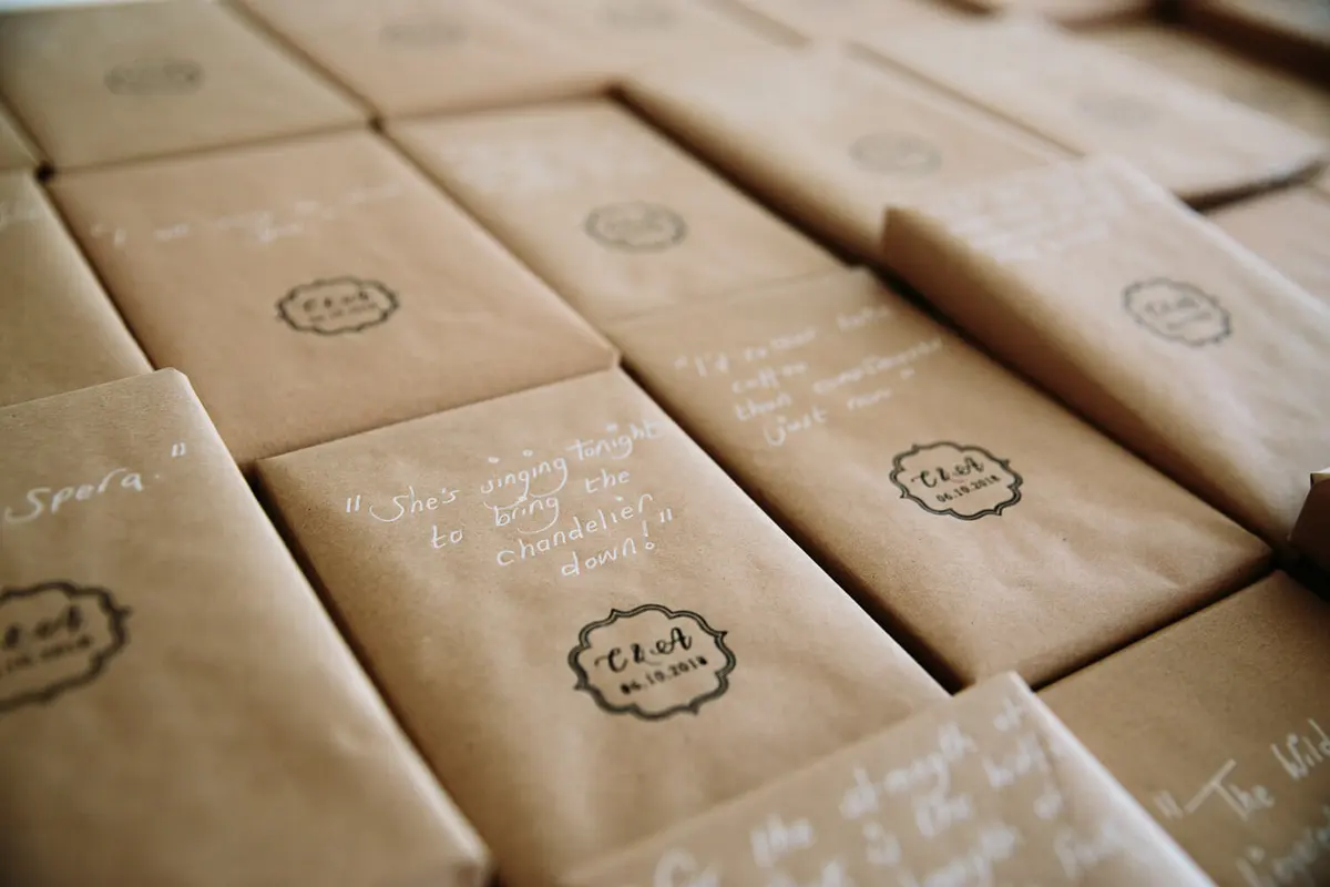 Rows of brown paper wrapped wedding favours with handwritten quotes and a stamped monogram