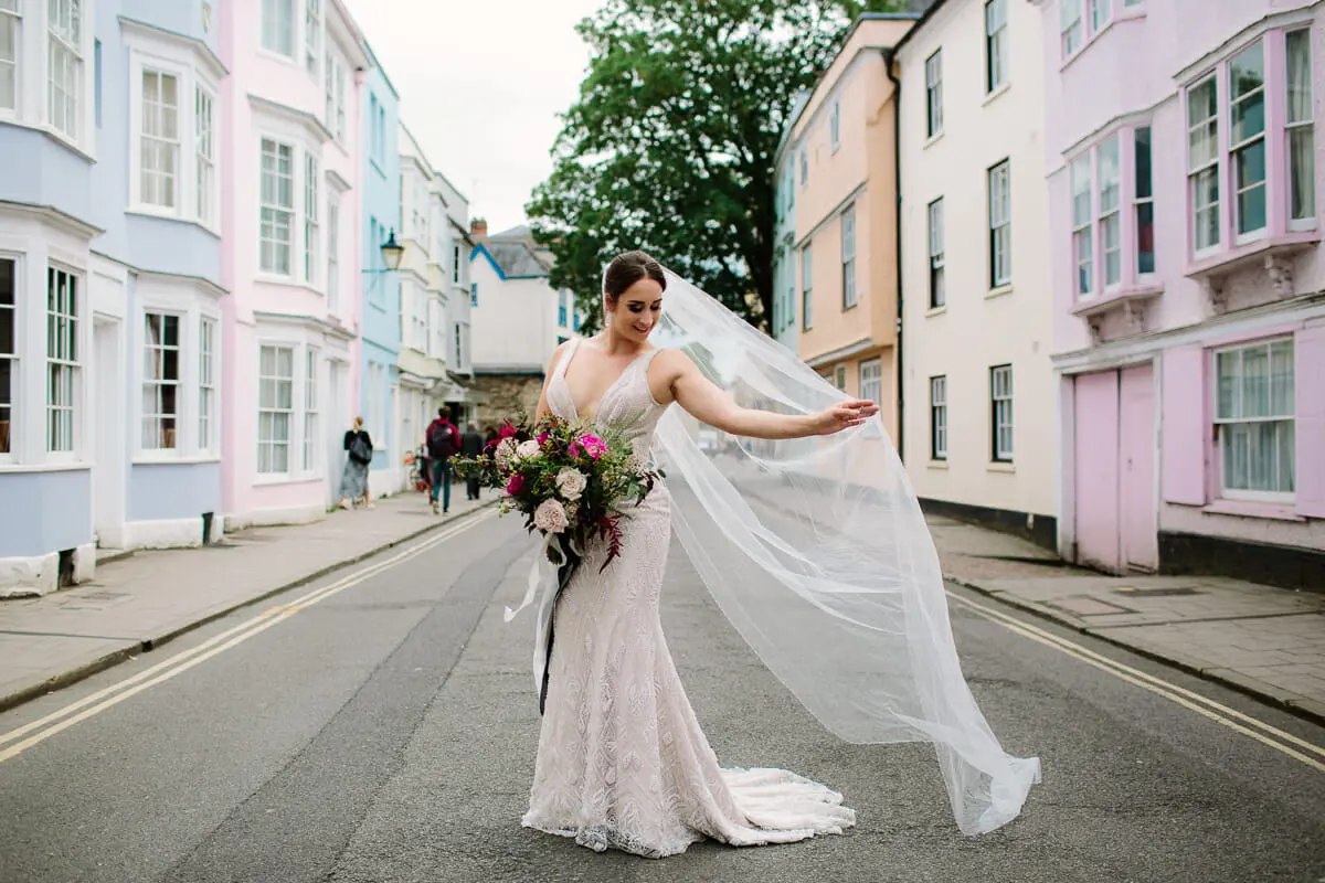 Bride twirling her long veil in the middle of a street lined with pastel-coloured houses