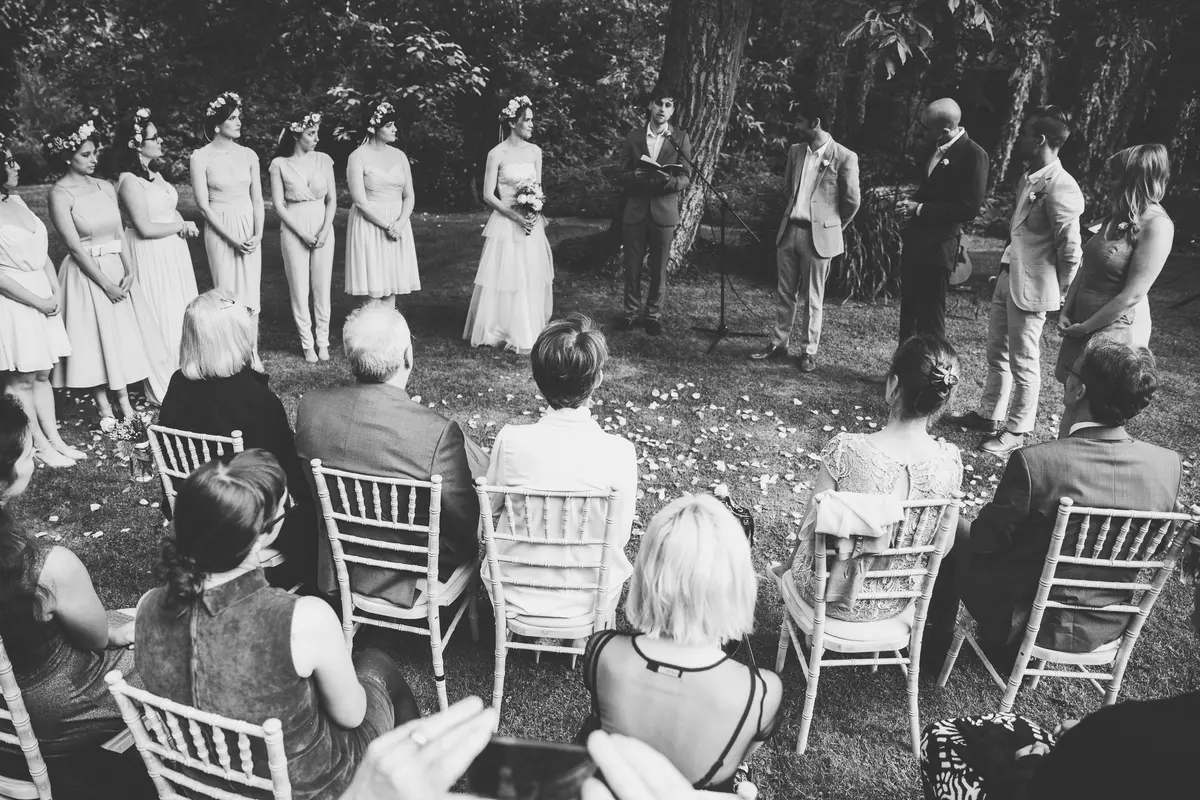 Black and white shot of guests watching an outdoor ceremony with bridesmaids in flower crowns