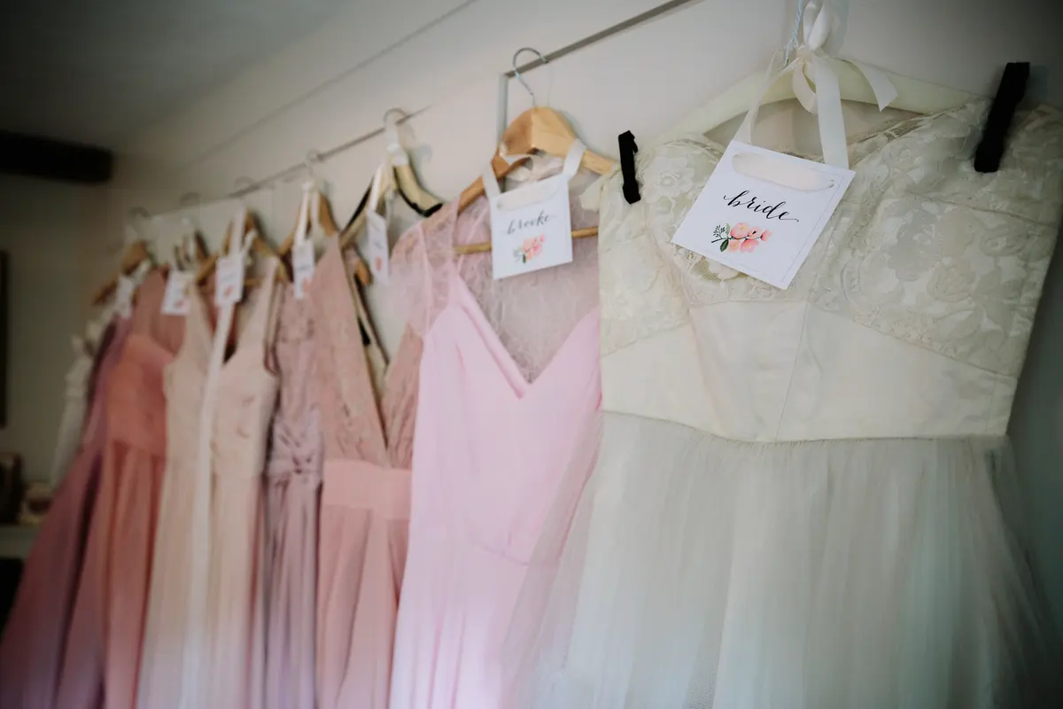 Pink bridesmaid dresses and a lace bridal gown hanging on a rail with name tags