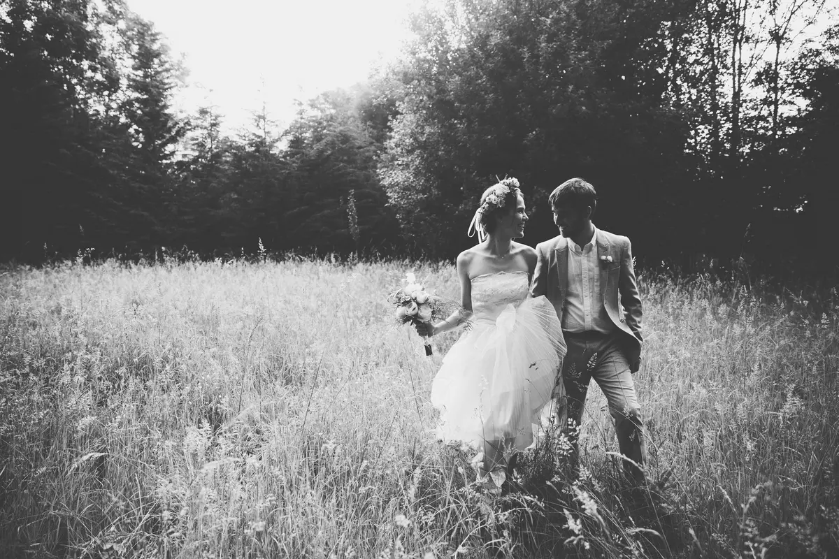 Black and white shot of the bride and groom walking through a meadow of long grass
