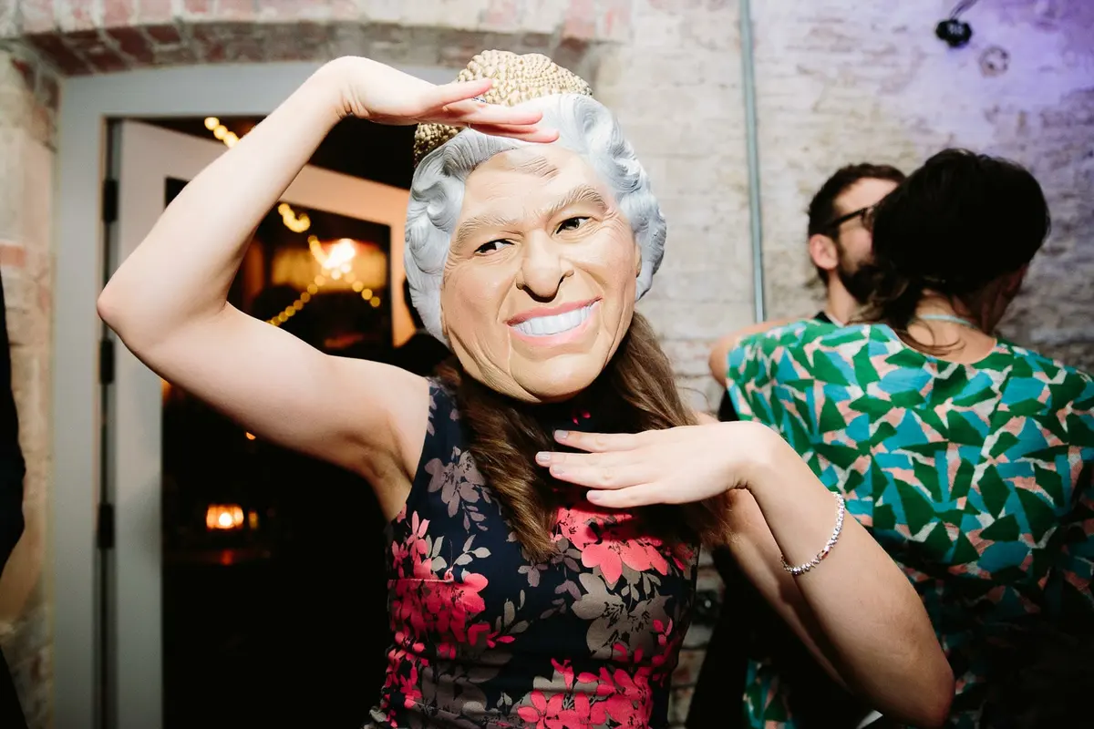 Wedding guest in a floral dress dancing in a rubber mask of the Queen