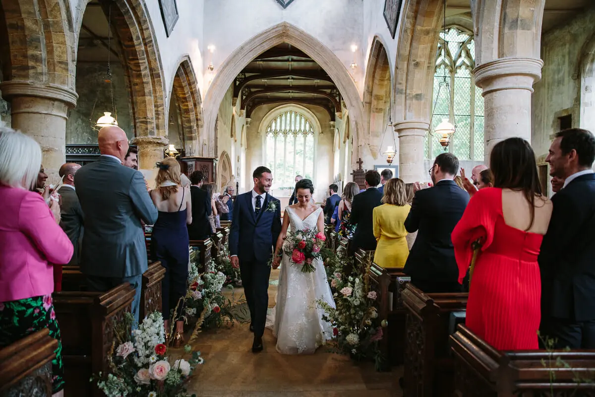 Bride and groom smiling as they walk back down the aisle of a stone church past guests