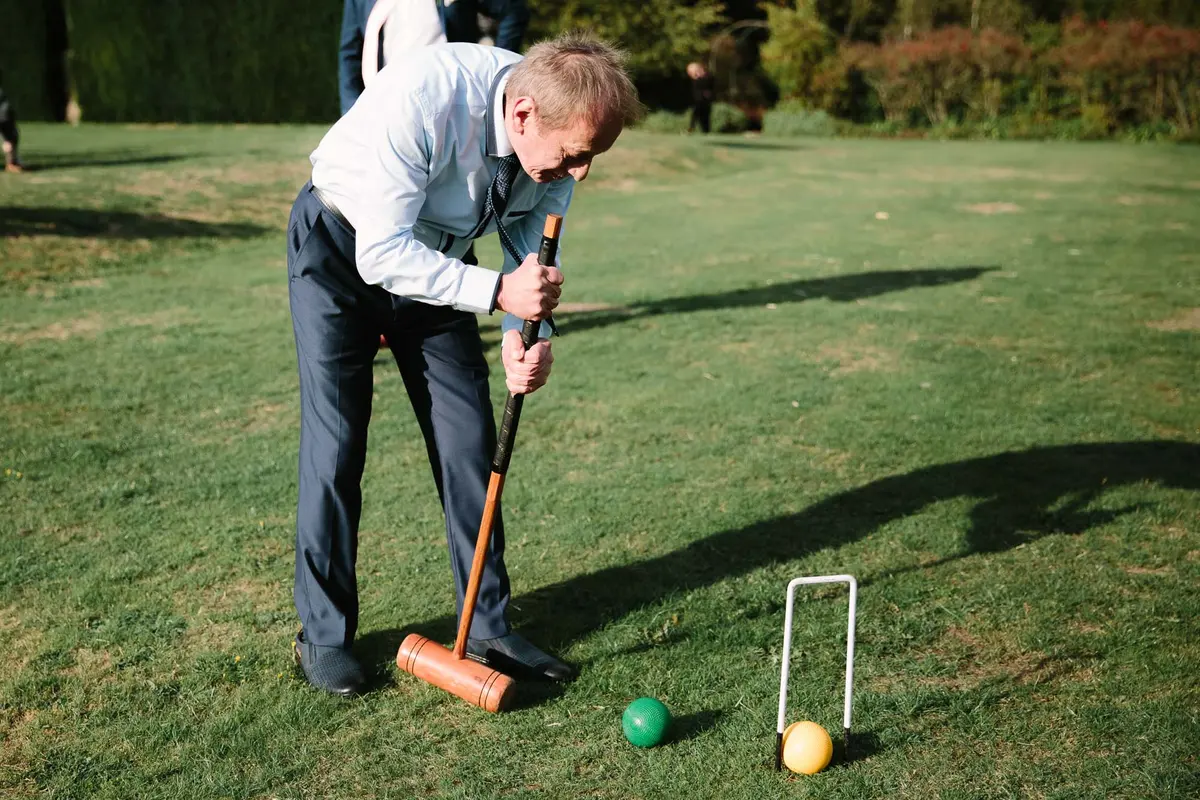 Wedding guest lining up a croquet shot on a sunny lawn