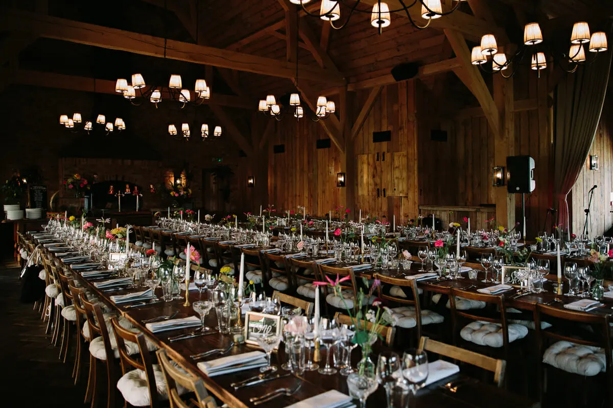Long tables set under chandeliers in the timber barn at Soho Farmhouse