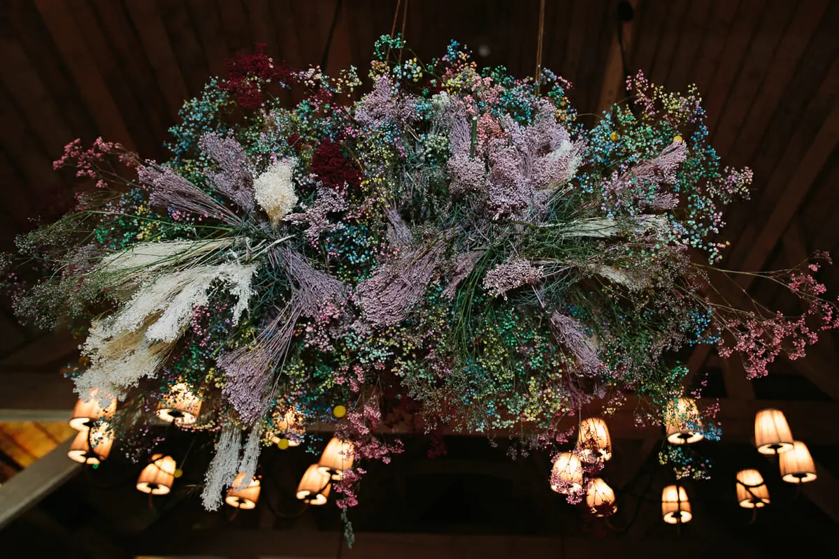 Suspended installation of dried flowers and grasses above chandeliers in the barn at Soho Farmhouse