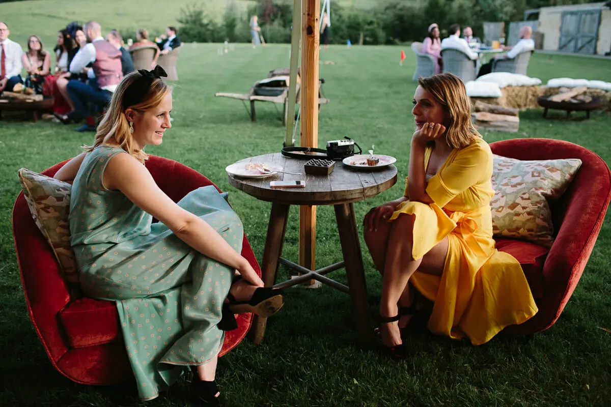 Two guests chatting in red velvet armchairs at a small table on the lawn