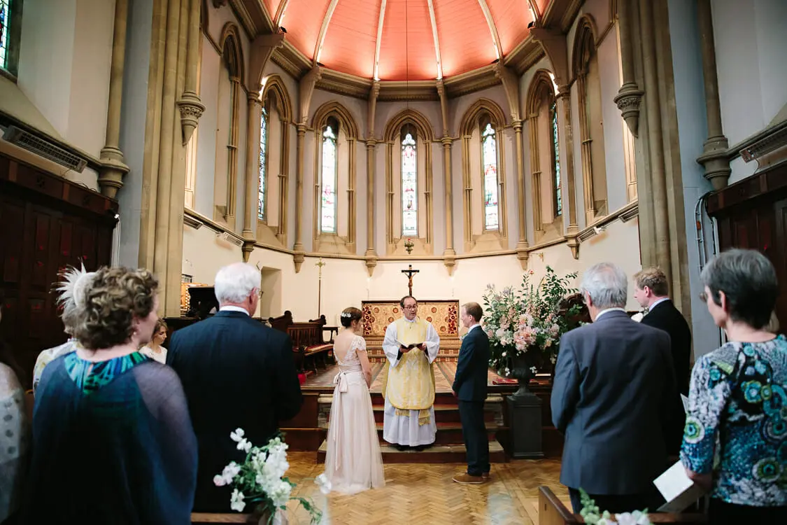 Bride and groom standing before the priest at the altar of a chapel with a painted domed apse