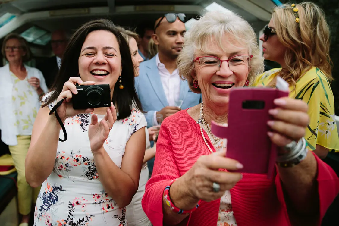 Two smiling wedding guests taking photos, one with a camera and one with a pink phone