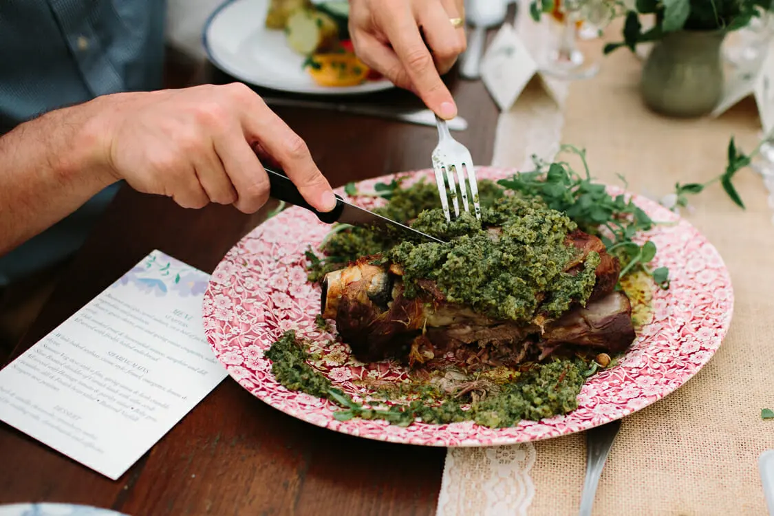 Guest cutting into a slow-roasted shoulder of lamb topped with herbs on a red patterned plate