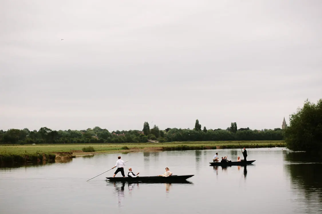 Two punts carrying wedding guests across a wide, still stretch of river beside meadows near the Perch