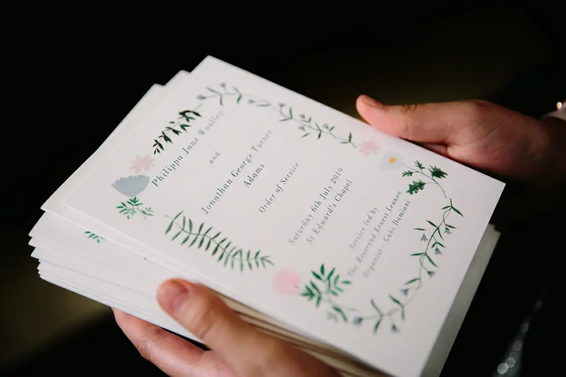 Hands holding a stack of orders of service decorated with painted leaves and flowers