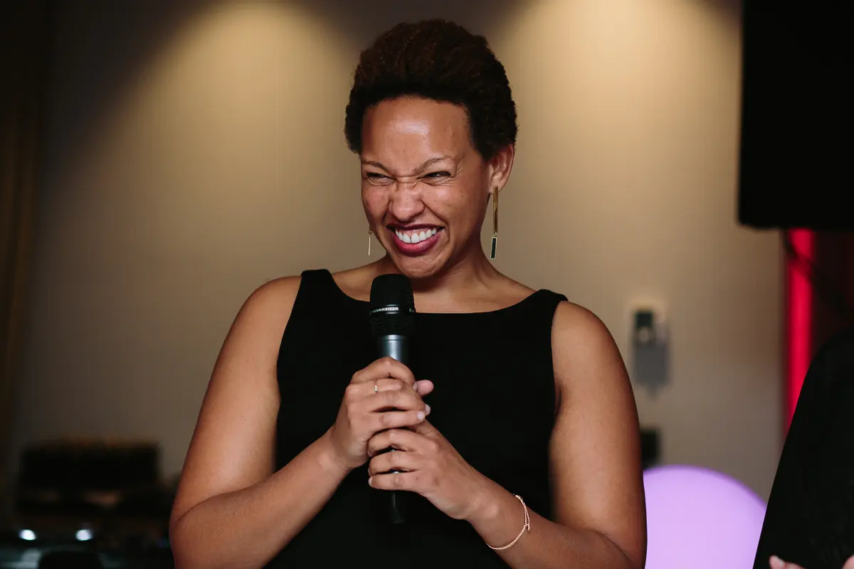 Guest in a black dress laughing as she gives a speech into a microphone