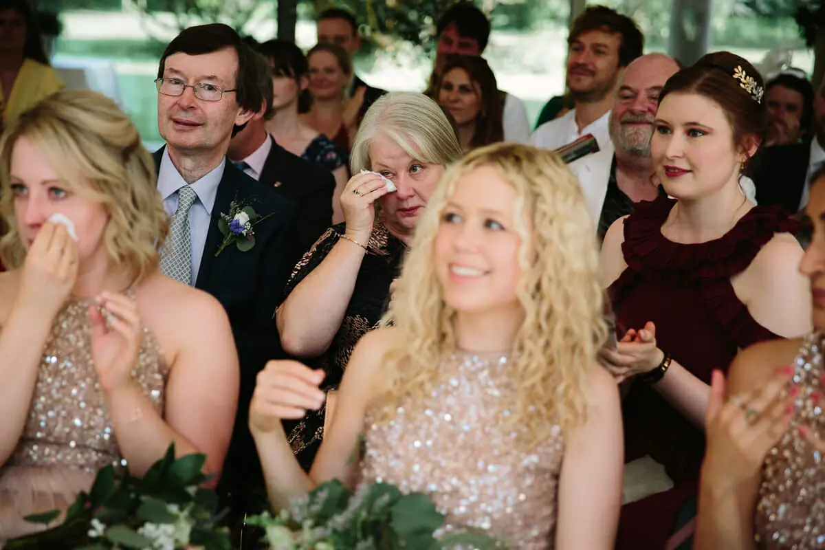 Bridesmaids in sequinned dresses and guests wiping away tears during the ceremony