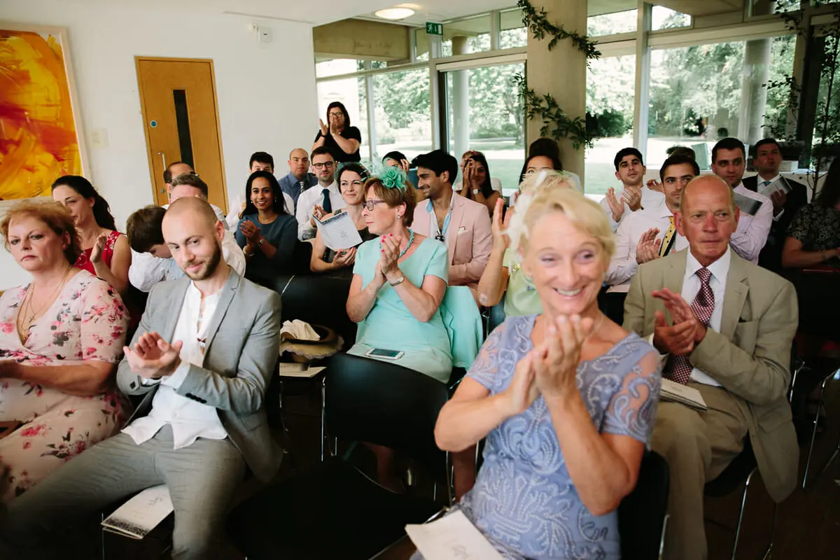 Smiling guests standing and applauding in a bright room with garden views