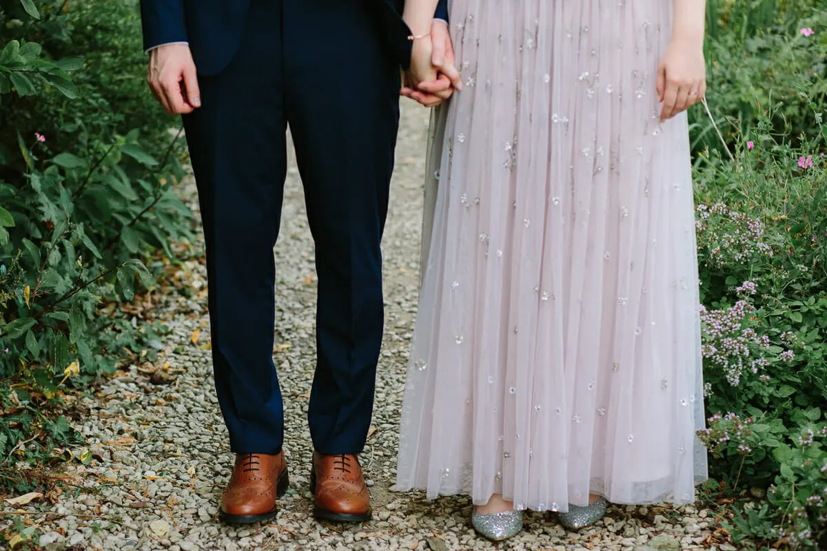 Groom in brown brogues and bride in a sparkly lilac gown holding hands on a gravel path