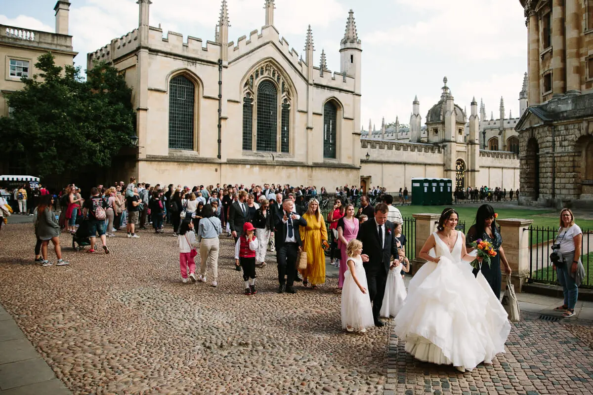 Bride walking across Radcliffe Square in Oxford with family and guests after the ceremony