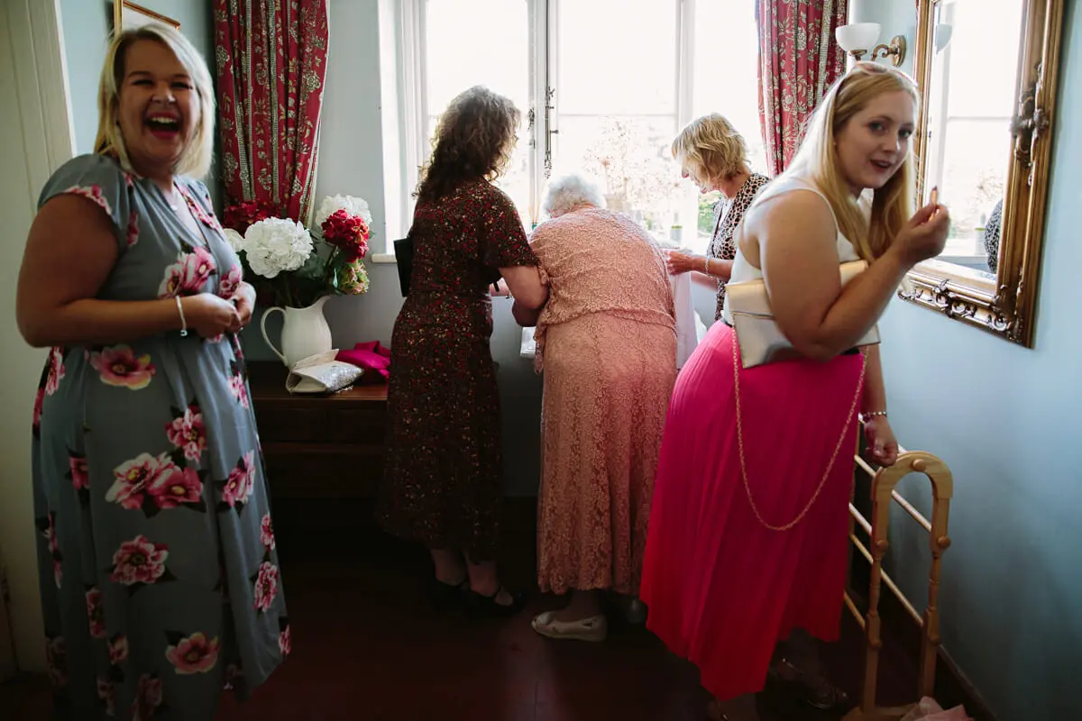 Laughing wedding guests in summer dresses gathered by a window in a hallway