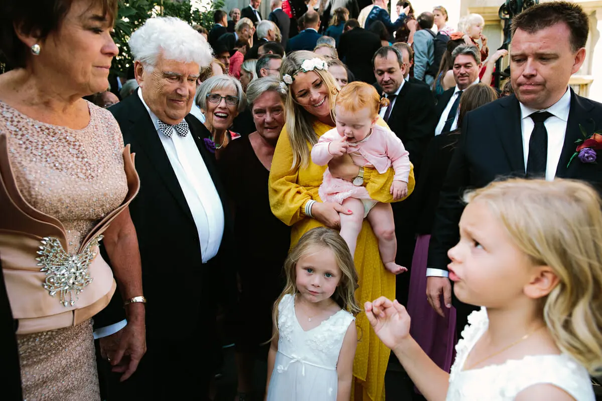 Crowd of guests gathered outside, with a woman holding a baby and a flower girl in front