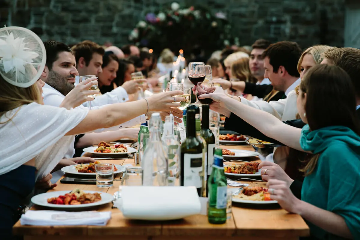 Guests raising their glasses in a toast across a long candlelit dinner table outdoors