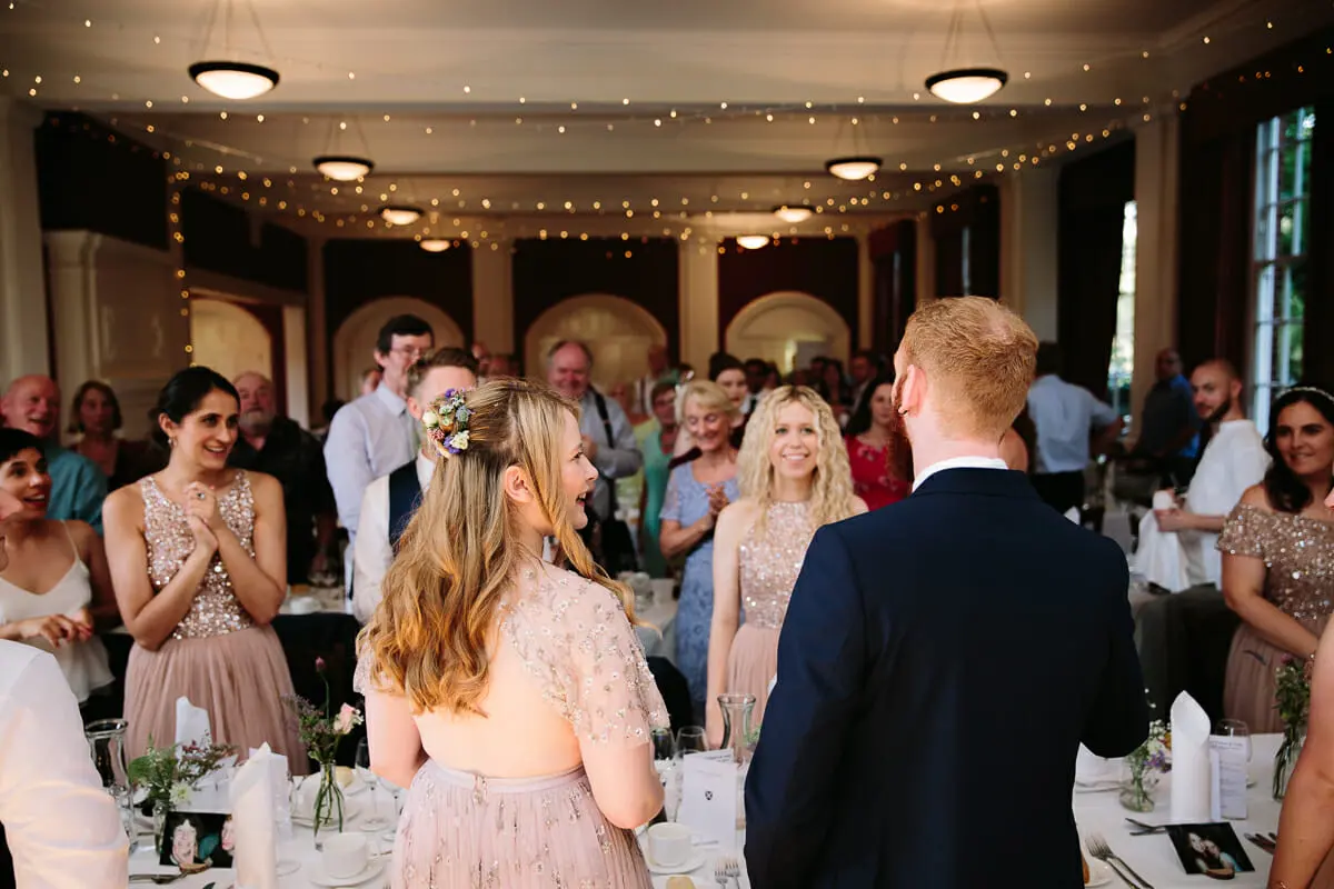 Bride and groom welcomed by clapping guests as they enter the reception room under fairy lights