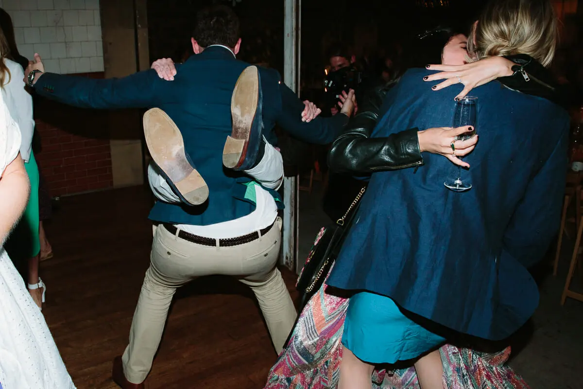 Guests dancing wildly at an evening reception, one man kicking his legs up as two women hug nearby
