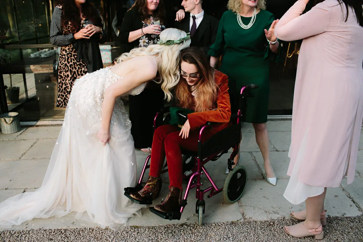 Bride bending down to hug a guest in a wheelchair outside the reception