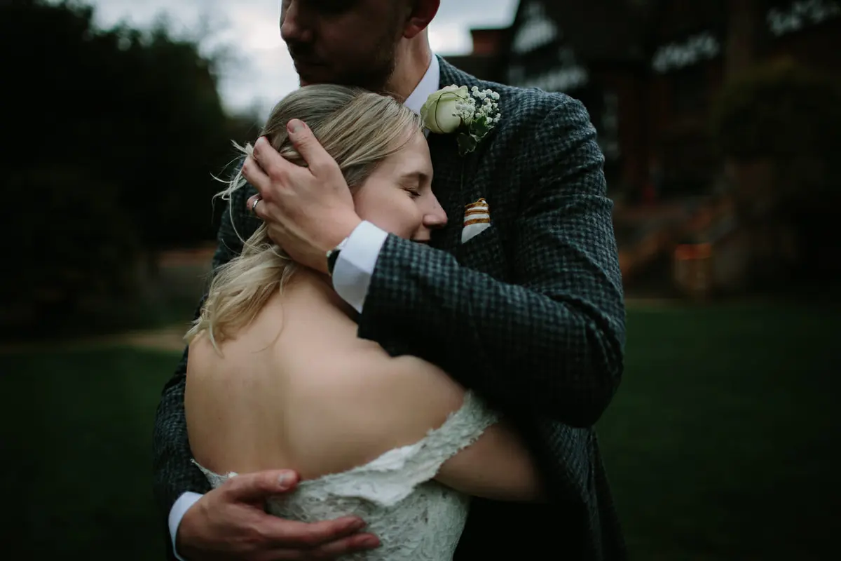 Groom holding the bride close as she rests her head against his chest outdoors at dusk