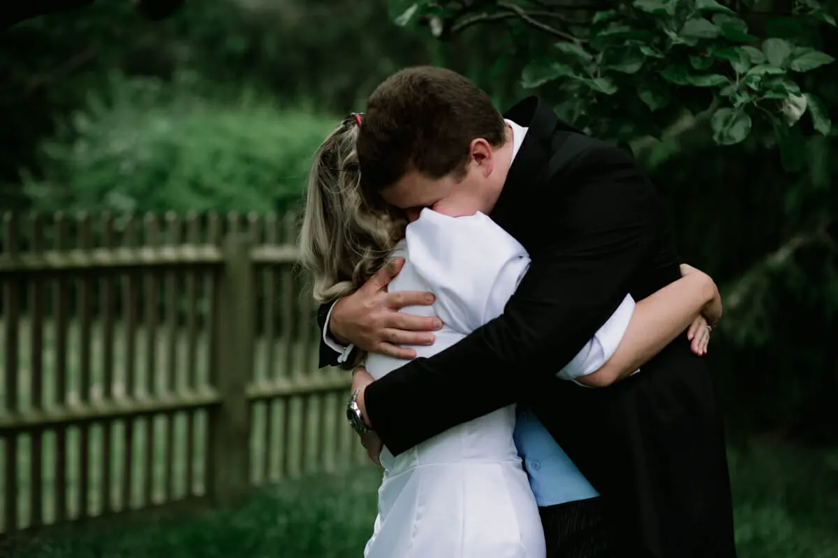 Couple holding each other in a tight hug in a garden beside a wooden fence