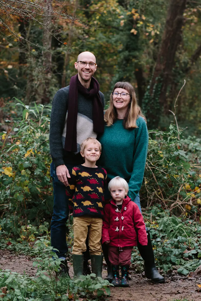 Family of four in wellies standing together on a woodland path in autumn