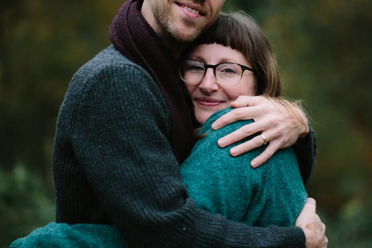 Couple in knitted jumpers sharing a close hug in autumn woodland
