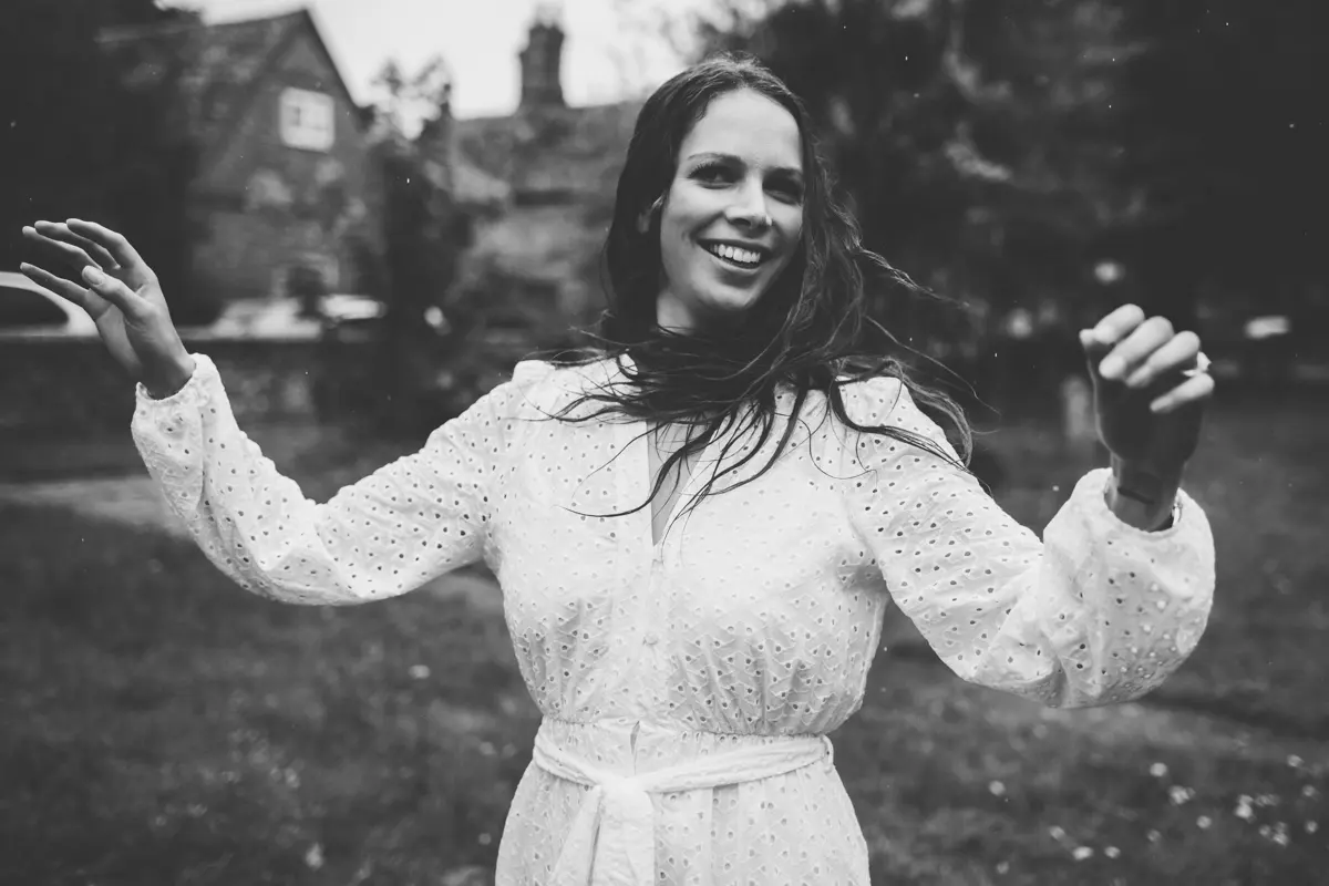 Black and white portrait of a smiling woman in a white dress dancing in a garden