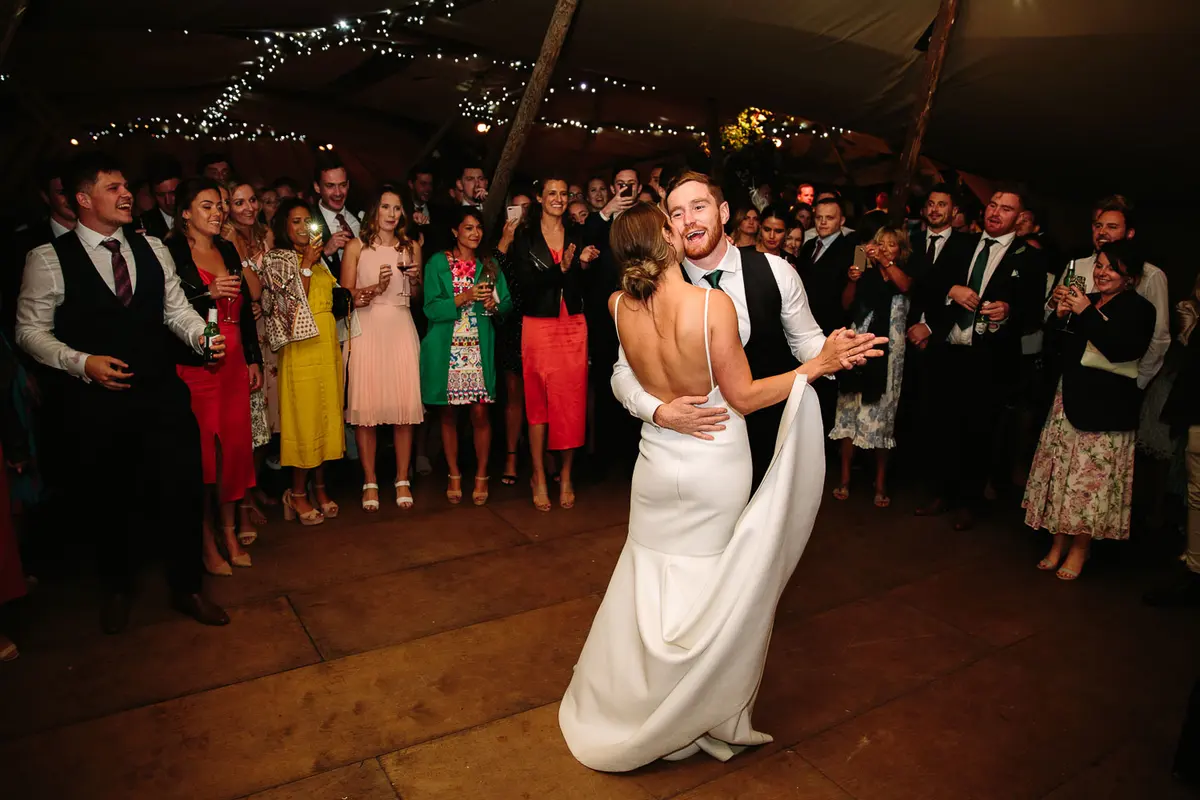 Bride and groom sharing their first dance in a tipi as guests gather round and cheer