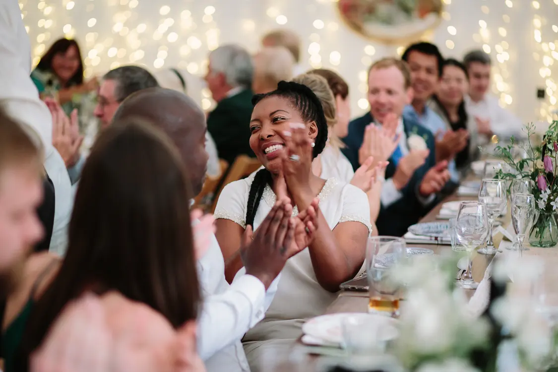Guest clapping and smiling during the speeches at a long table under fairy lights