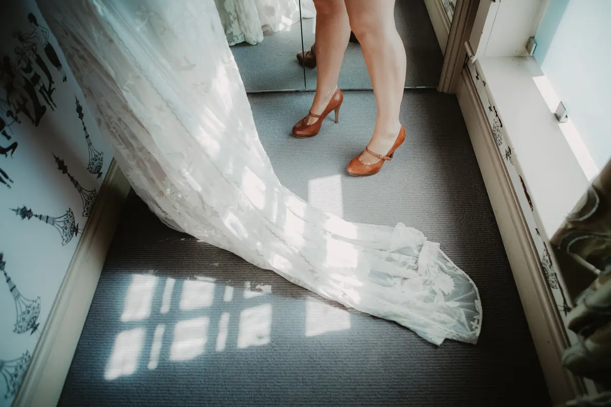 Bride in tan heels with the lace train of her dress spread across the floor in sunlight