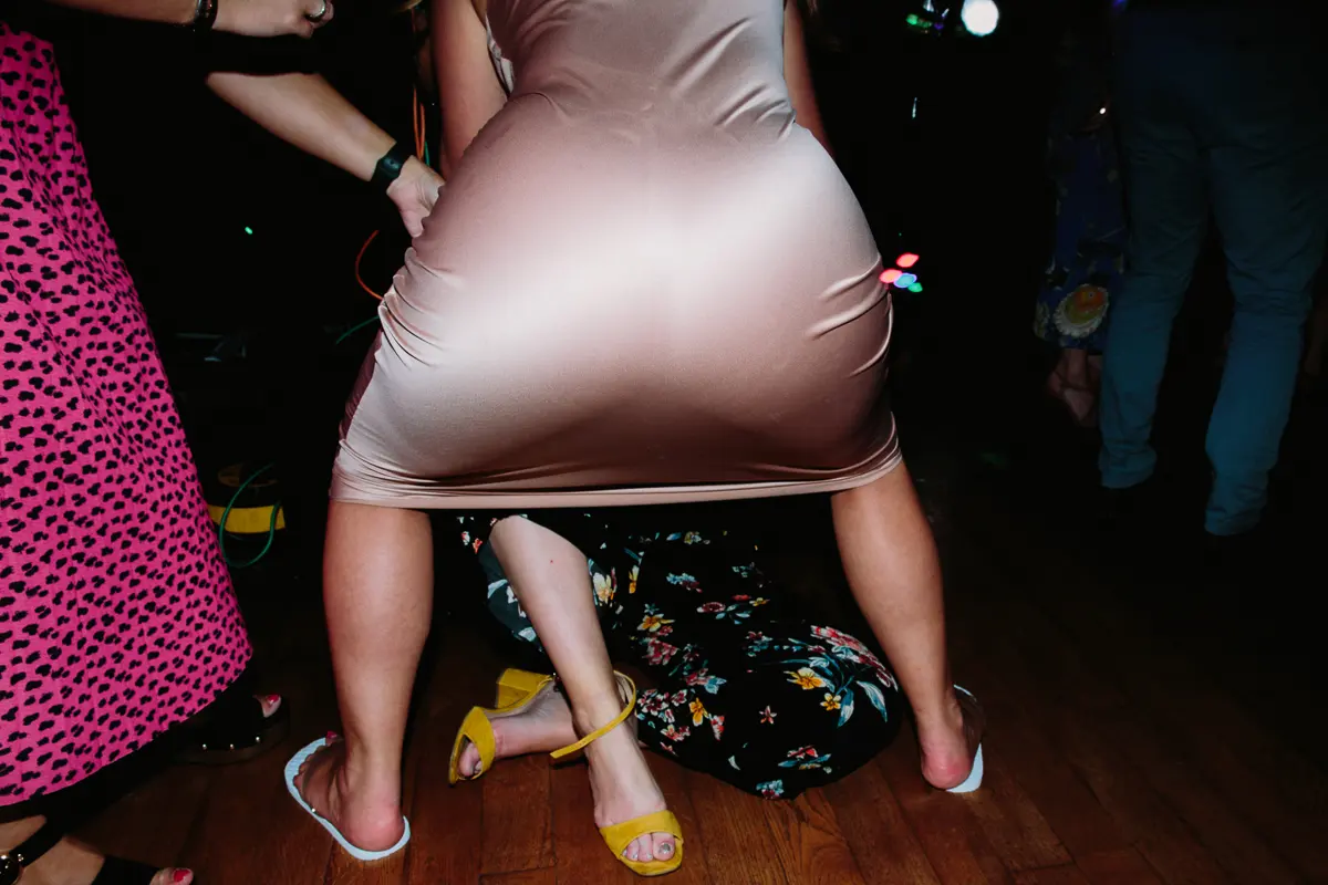 Guest in a satin dress straddling a friend lying on the dance floor as others laugh
