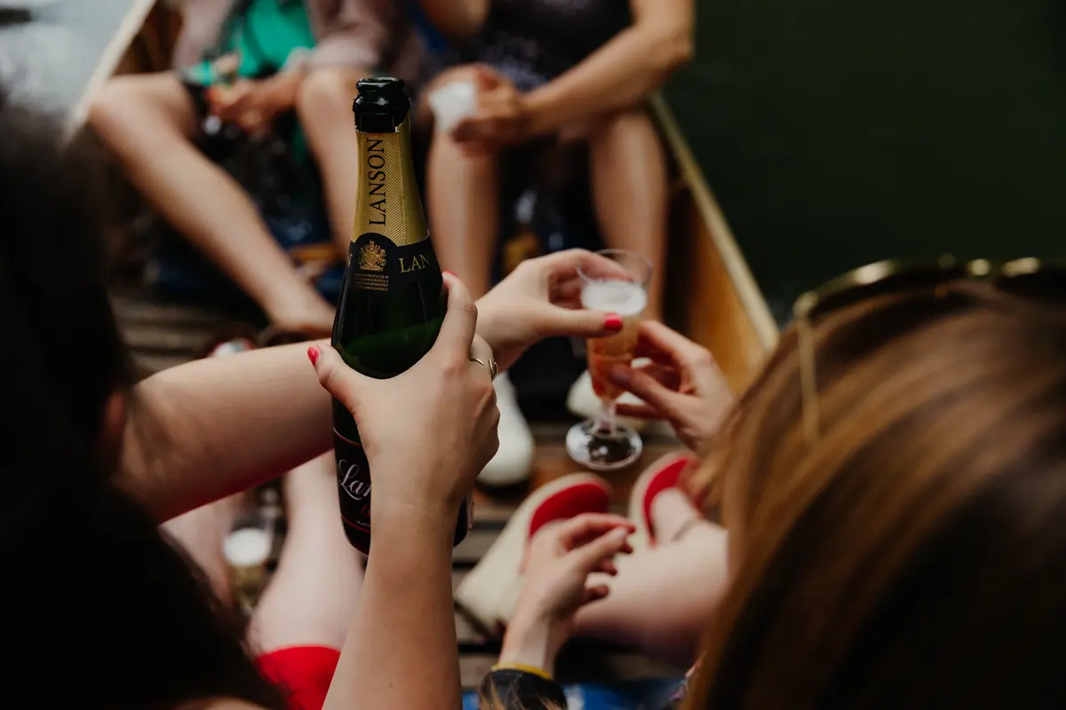 Guest pouring Champagne into a glass for friends sitting in a punt