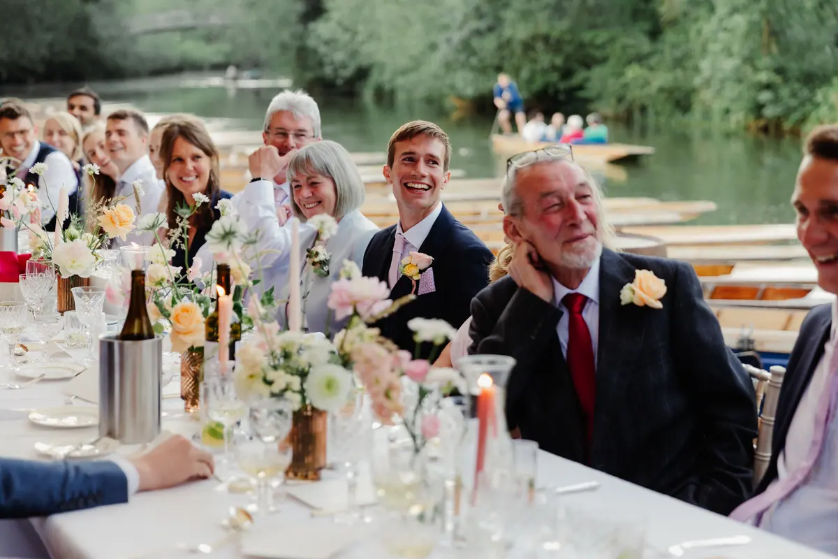 Guests laughing at a long table during the speeches, with punts on the river behind at Cherwell Boathouse