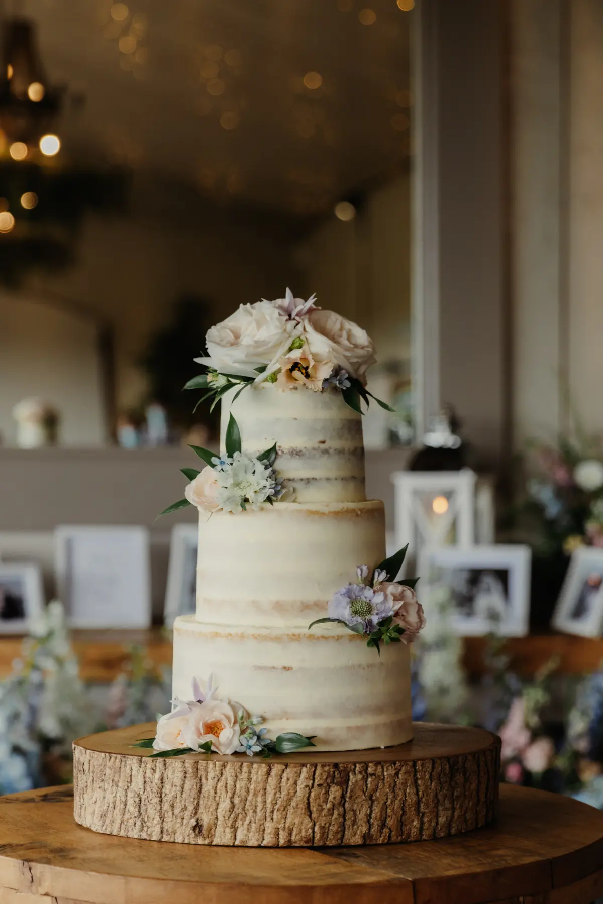 Three-tier semi-naked wedding cake with roses and pale flowers on a log slice stand