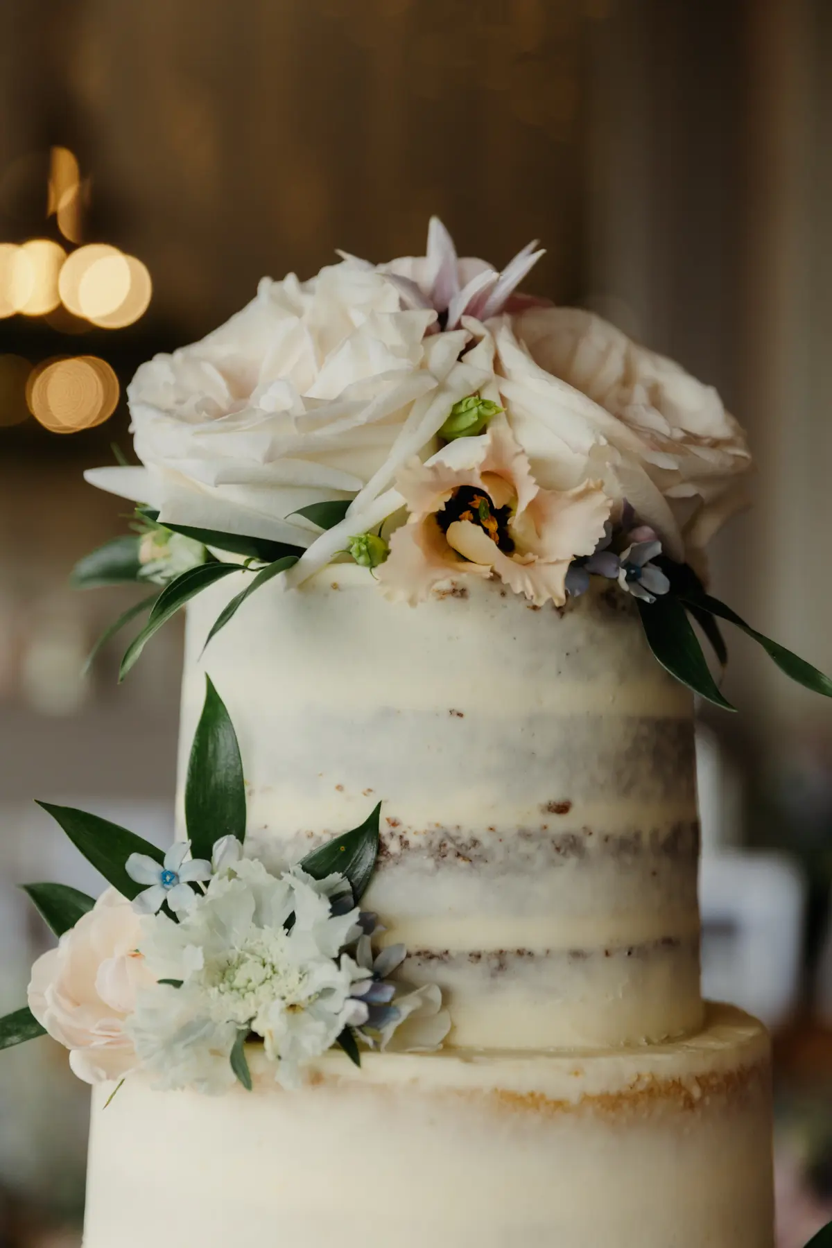 Close-up of the top tiers of a semi-naked wedding cake decorated with roses and blue flowers