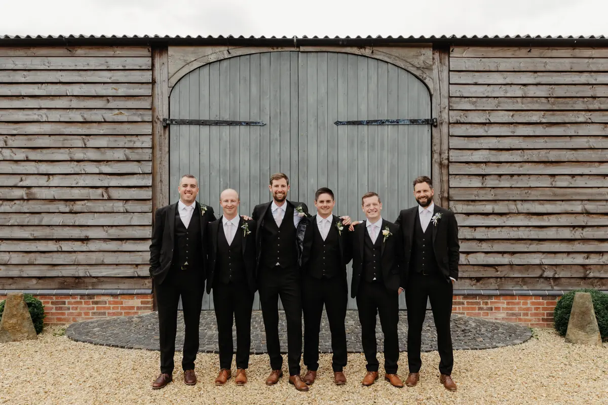 Groom and groomsmen in dark suits standing in front of the barn doors at Primrose Hill Farm