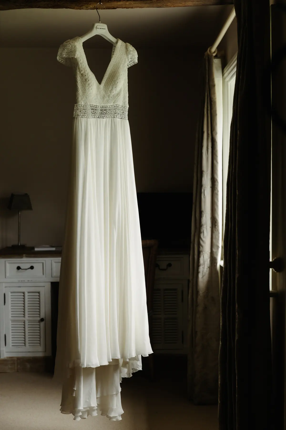 Wedding dress with a lace bodice hanging on a hanger in a dim bedroom