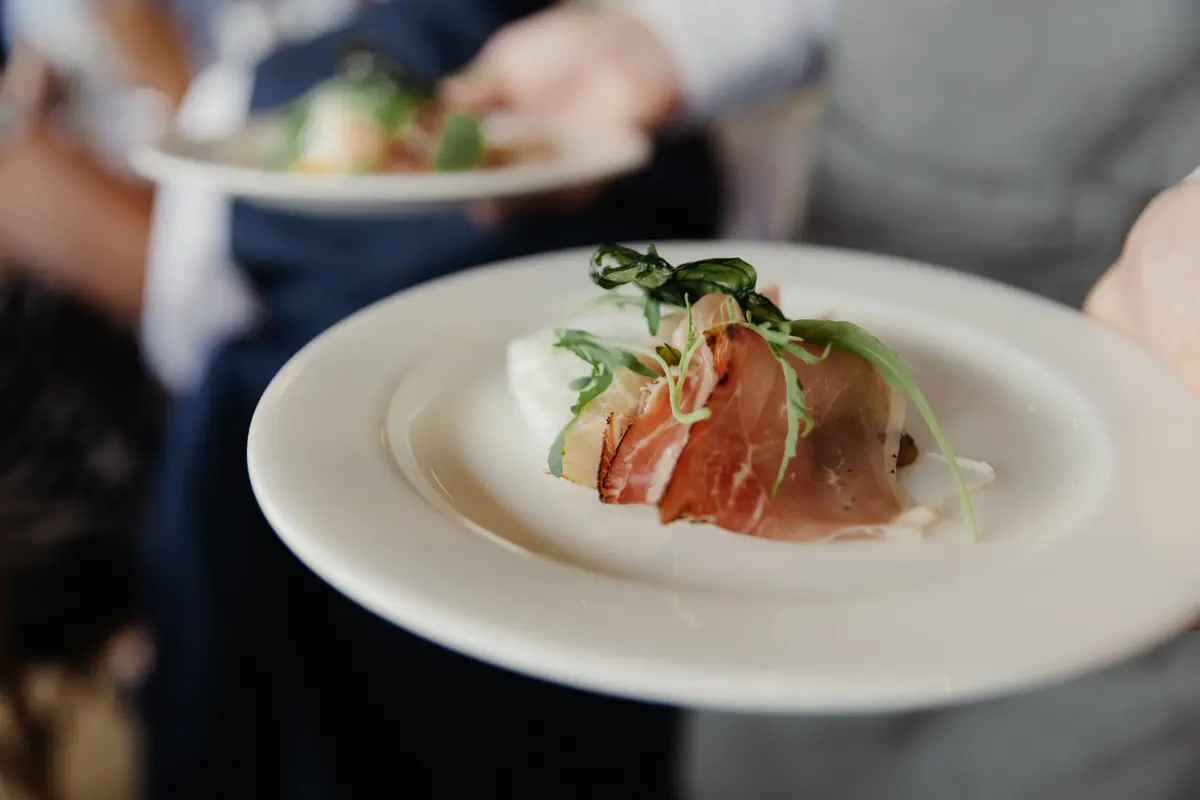 Plate of cured ham with rocket and mozzarella being carried to the tables by waiting staff