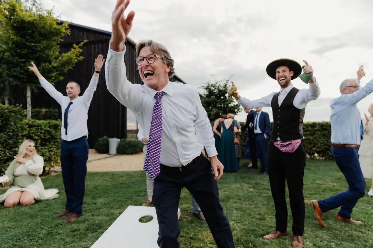 Guests cheering and raising their arms during a game of cornhole on the lawn