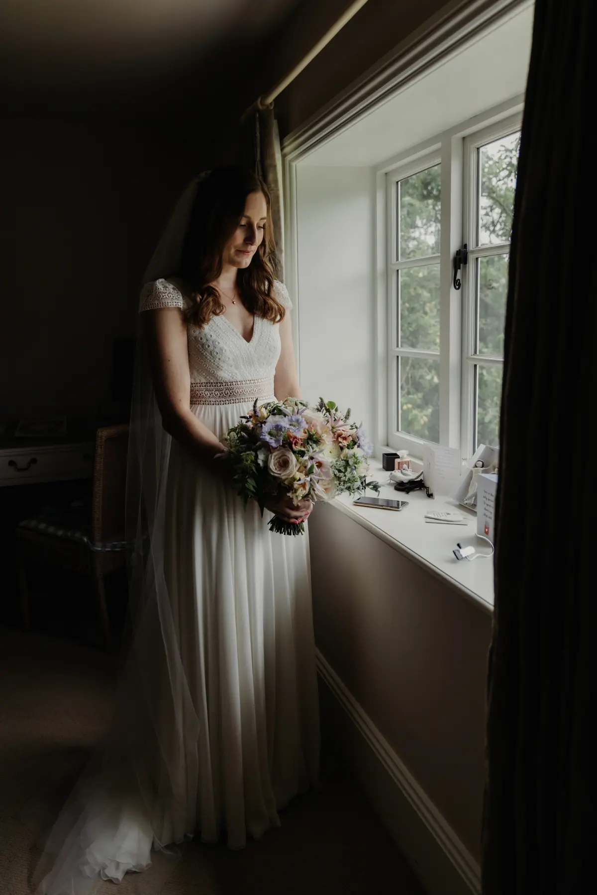 female bride stood by window wearing white wedding dress
