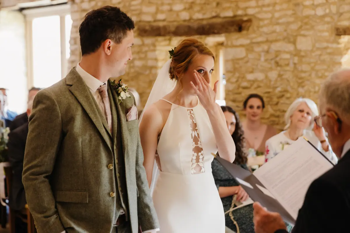 Bride wiping away a tear beside the groom as a reading is given during the ceremony at Caswell House