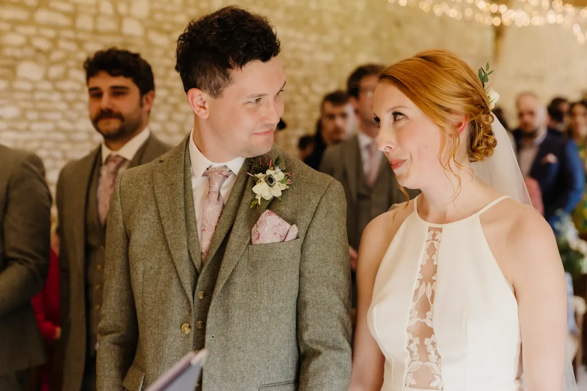 Bride smiling up at the groom in a tweed suit during the ceremony at Caswell House