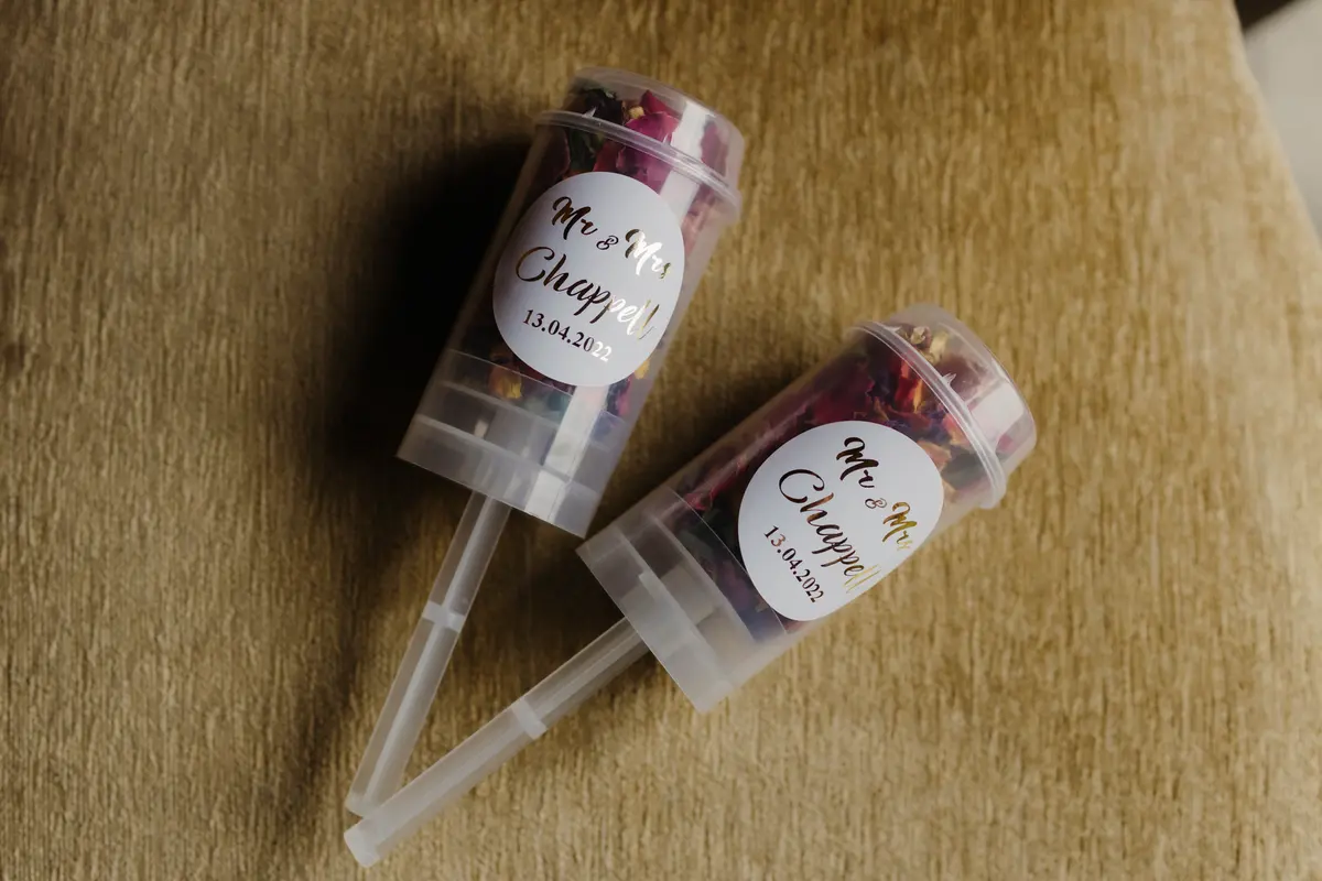 Two petal confetti cannons with personalised gold labels lying on a velvet chair at Caswell House