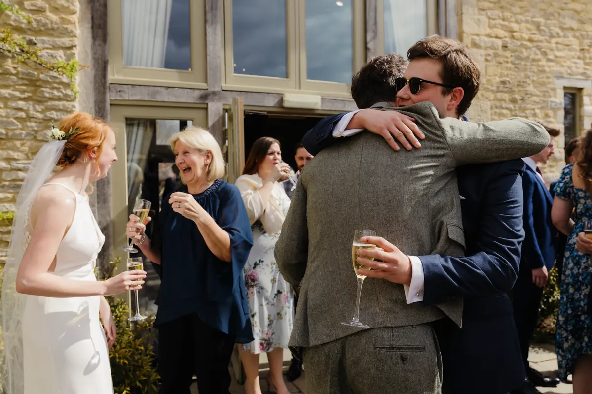 Groom hugging a friend while the bride laughs with a guest outside Caswell House